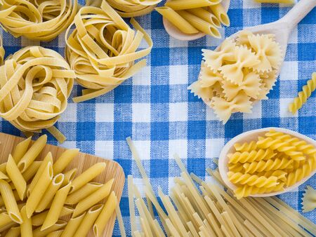 Colorful and stylist composition. Mixed dried pasta selection on blue and white linen towel as background. Flat lay top view with copyspace for text, logo or other. Cooking and Italian foods concept.の写真素材