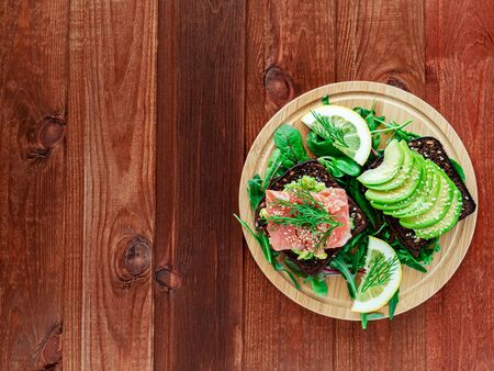 Clean eating. Healthy avocado toasts for breakfast or lunch at quarantine with rye bread, arugula, charg, sliced avocado, guacamole, salmon, lemon and sesame. Top view. Mexican cuisine. Stay home.の写真素材