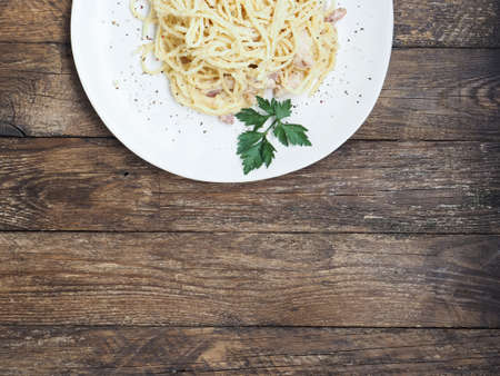 Traditional italian cuisine. Classic hoemade pasta carbonara. Spaghetti with bacon, egg yolk and parmesan cheese on light plate on dark wooden background. Top view with copy space.の写真素材