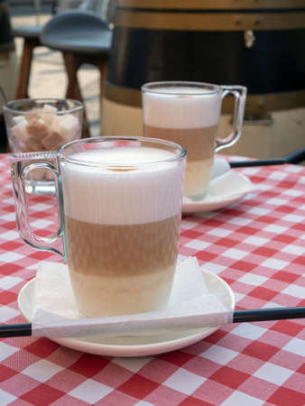 Cafe and bar, barista art concept. Frothy, layered cappuccino in a clear glass mug. Tempting coffee latte in two tall glasses in coffee house.の写真素材