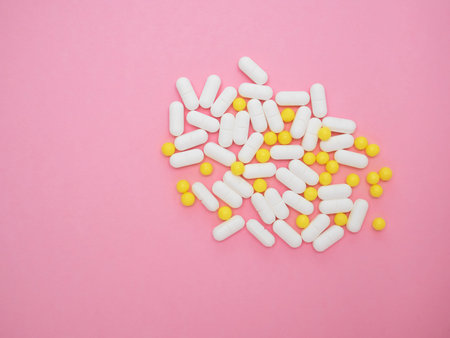 Colorful and stylish composition. Heap of white and yellow pills on pink paper background. Assortment of medicinal pharmaceutical products. Concept of healthcare and medicine. Treatment of viruses.の写真素材