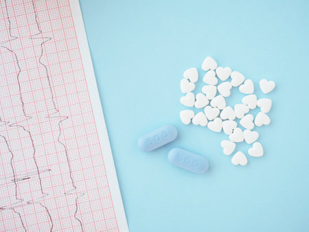 Concept of cardiology, medicine and insurance. White pills in form of heart and blue tablets with sign 500 on blue background with electrocardiogram paper. Medications for cardiac patients. Top view.の写真素材