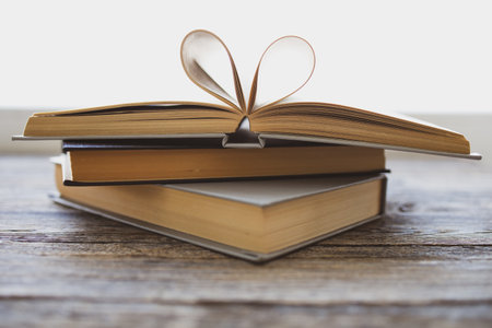Composition of love with open book heart. Old books on a wooden table. Pages of the book in the form of heart. Heart shape for love in valentine day with blurred background. Vintage color tone style.の写真素材