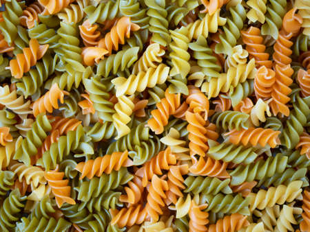 Three Colors Rotini Pasta. Pasta fusilli tricolore background. Abstract texture of colorful pasta. Pattern of macaroni. Bright multicolor food backdrop. Uncooked colored noodles.の写真素材