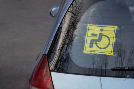 Attention sign, disabled person inside. Yellow and black sticker with a wheelchair symbol on stuck to the inside of the rear car window. Close upの写真素材