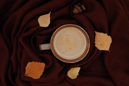 Atmospheric Autumn or Fall morning coffee in warm colors. Fall yellow leaves, acorn, hot cup of black coffee and cozy brown scarf as background. Sunday relaxing, autumn mood and still life concept.の写真素材