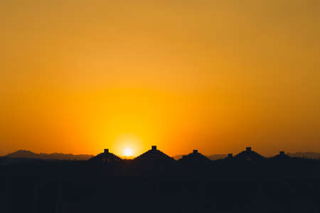 Majestic dusk in tropics. Goden sunset sky with beautiful silhouette roofs beach umbrellas and mountains in the evening. Warm orange colors. Abstract nature and travel background. Egypt summer.の写真素材