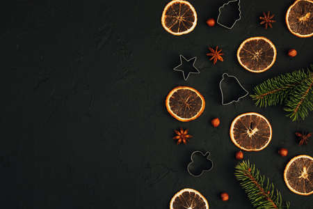 Christmas food dark background. Fir branches with cookie cutters, dry orange chips, anise and nuts. Top view. Culinary composition. Holiday card for the New Year 2022. Flat lay. Copy spaceの写真素材