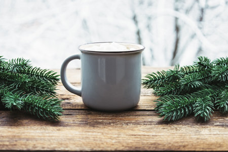 Grey cup with chocolate or cocoa, marshmallow and fir tree decoration on wooden table against backdrop of treess with snow on cold winter day. Hot warm drink in frosty weather. Cozy composition.の写真素材