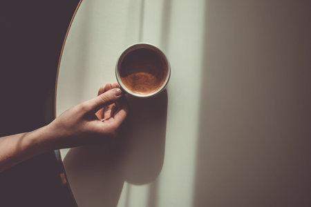 Woman hand with cup of americano or expresso on the white table. Morning coffee concept. Sunday...