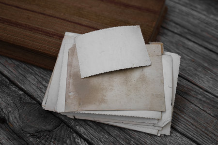 Family traditions, memory and nostalgia concept. Clear blank photo frames to placed your pictures or text with photo album on wooden board background in retro style. A stack of old photos.の写真素材