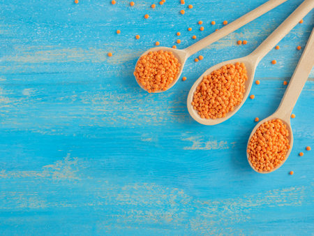 Three wooden spoons with Red Lentils or Masoor Dal on light blue background. Flat lay. Colorful and stylish composition. Vegetarian super food. Healthy eating and dietary. Canadian Orange Lentilの写真素材