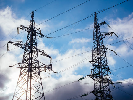 High voltage electricity pillars on the blue sky background with clouds. Metal bearing high voltage power line. High tech power linesの写真素材