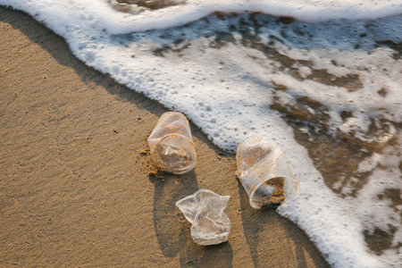 Discarded to beach of sea three plastic cups . Environmental and coast pollution. Used disposable tableware thrown on the seashore. Threat the health of ocean. Waste during peoples vacationの写真素材