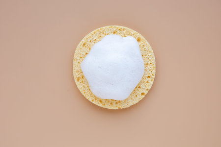 Natural facial cosmetic sponge with cleansing foam on pastel background. Morning or evening beauty...