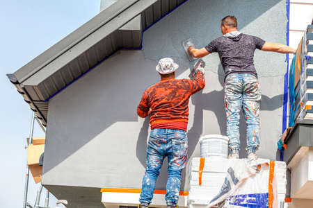 Construction workers plaster the facade of the house. Application Of Facade Plaster. Elevation of the building. Four workers are plastering the facade of the building.の写真素材