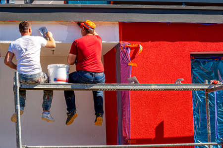 Construction workers plaster the facade of the house. Application Of Facade Plaster. Elevation of the building. Four workers are plastering the facade of the building.の写真素材