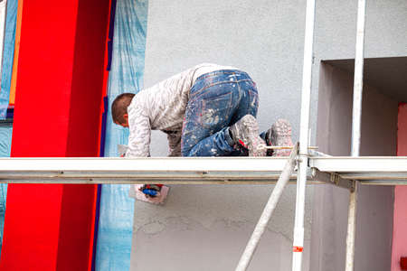 Construction workers plaster the facade of the house. Application Of Facade Plaster. Elevation of the building. Four workers are plastering the facade of the building.の写真素材