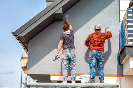 Construction workers plaster the facade of the house. Application Of Facade Plaster. Elevation of the building. Four workers are plastering the facade of the building.の写真素材
