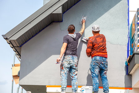 Construction workers plaster the facade of the house. Application Of Facade Plaster. Elevation of the building. Four workers are plastering the facade of the building.の写真素材
