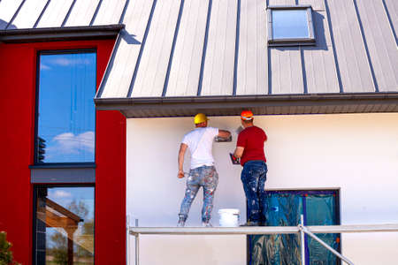 Construction workers plaster the facade of the house. Application Of Facade Plaster. Elevation of the building. Four workers are plastering the facade of the building.の写真素材