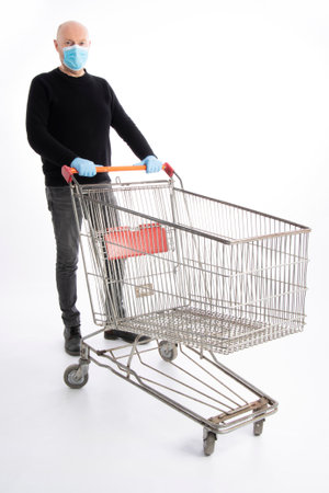 Man with mouth protection and hand gloves pushing a shopping cart, isolated on white backgroundの写真素材