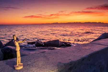 Wooden Human Manikin posing on beach at sunrise with a view of False Bay on a beautiful cloudy...