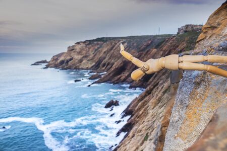 Wooden Human Manikin posing on a cliff with a beautiful misty sea from a view point on a beach in Mossel Bayの写真素材