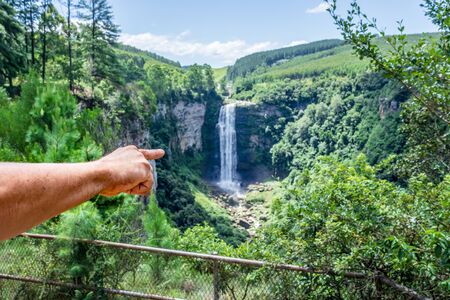 Caucasian male hand pointing at a large waterfall and river, vegetation and mountains, Pietermaritzburg , South Africaの写真素材