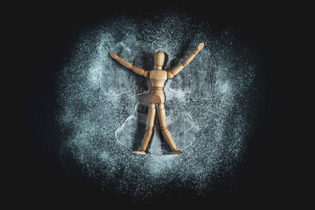 Wooden Human Manikin lying in white snow powder making snow angels with a black background