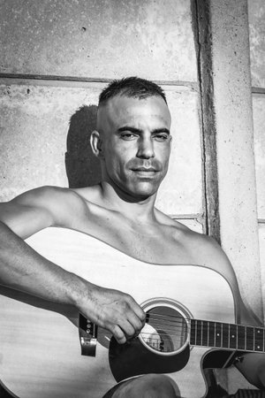 Portrait of a handsome Caucasian man playing an acoustic guitar in black and white