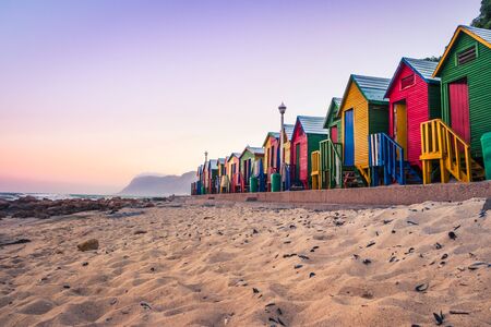 View of the beautiful sunset over False Bay from Kalkbay with little coloured houses on the beach, with mountains in the background, Cape Town, South Africaの写真素材