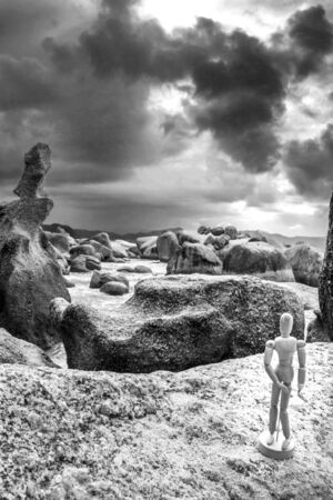 Wooden artist manikin posing during a sunrise on a cloudy morning from the rocks on Boulders beach, Simon's Town, Cape Town, South Africaの写真素材