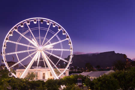 View of Table Mountain and a big white Ferris wheel located at the waterfront at sunset on a beautiful calm evening, Cape Town, South Africaの写真素材