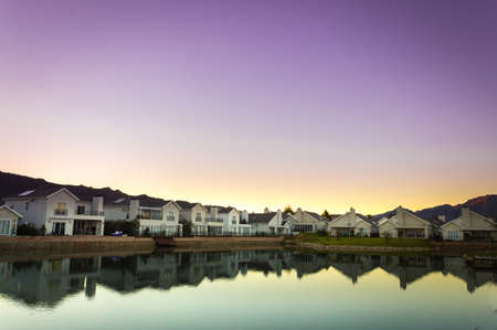 A row of houses surrounding a lake filled with reflections of the houses at sunrise, Val de Vie, Cape Town, South Africaの写真素材