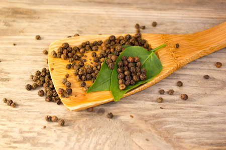 Black pepper in spoon and leaf on wooden backgroundの写真素材