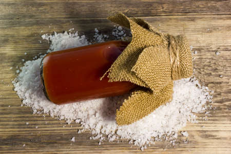 Tomato juice in glass bottle and big sea salt on wooden backgroundの写真素材