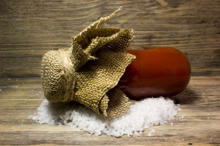 Tomato juice in glass bottle and big sea salt on wooden backgroundの写真素材