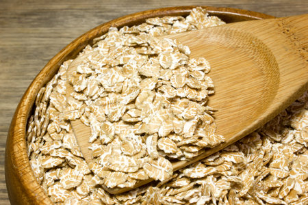 Wheat flakes in wooden spoon on wooden background