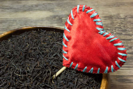 Dry tea leaves for black tea and red heart love on wooden backgroundの写真素材