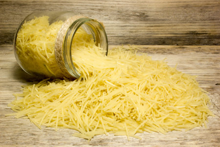 Small dry pasta noodles and glass jar on wooden background