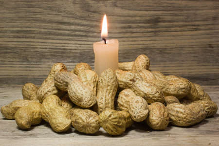 Peanuts in shell and burning candle on wooden backgroundの写真素材