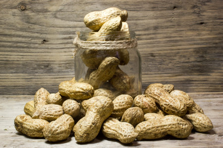 Peanuts in shell and glass jar on wooden background