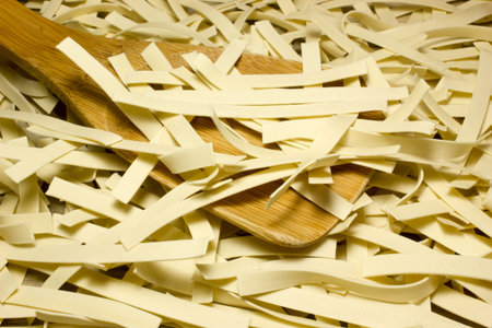 Wide Italian noodles and wooden spoon on wooden background