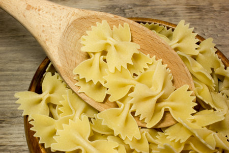 Noodles Farfalle butterflies and wooden spoon on wooden background.