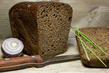 Black rye bread with knife on wooden background.
