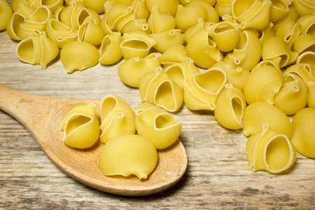 Noodles seashells and wooden spoon on wooden background