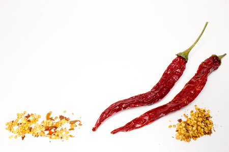 Chili peppers and seeds in wooden spoon on white background