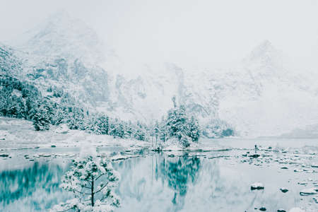 Turquoise surface of the mountain lake. Winter fabulous forest lake. Snow rocks and coniferous trees. The reflection in the mirror of water.の写真素材