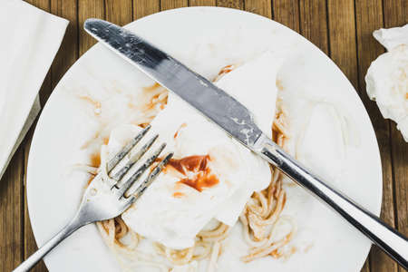 Remains of spaghetti, fork and knife on a white plate. Leftover food on a plate at the restaurant. The completion of dinner.の写真素材